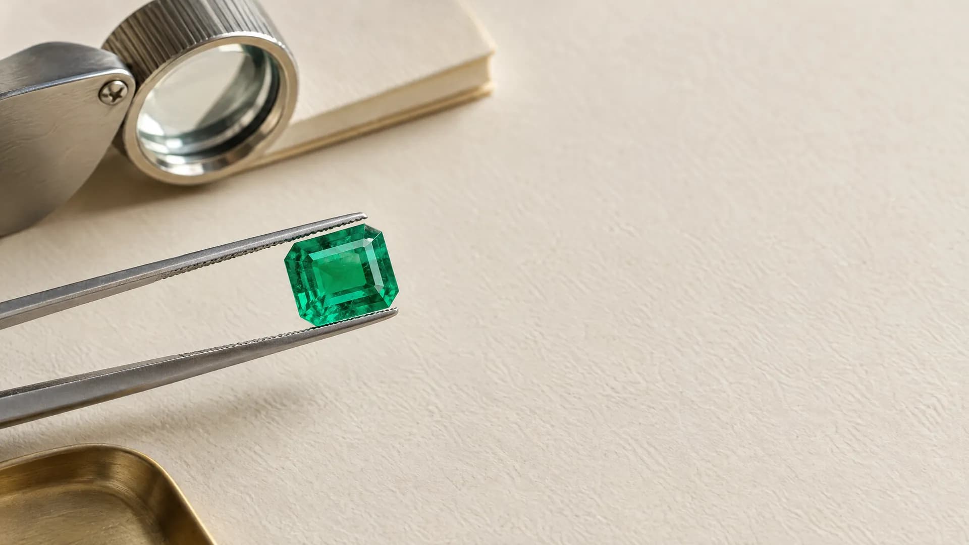 An emerald held in steel tweezers under a jeweller's loupe